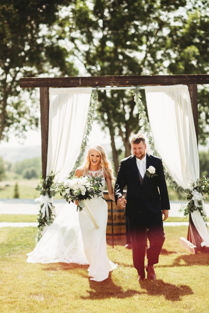Newly married couple walking away from outdoor wedding arch.