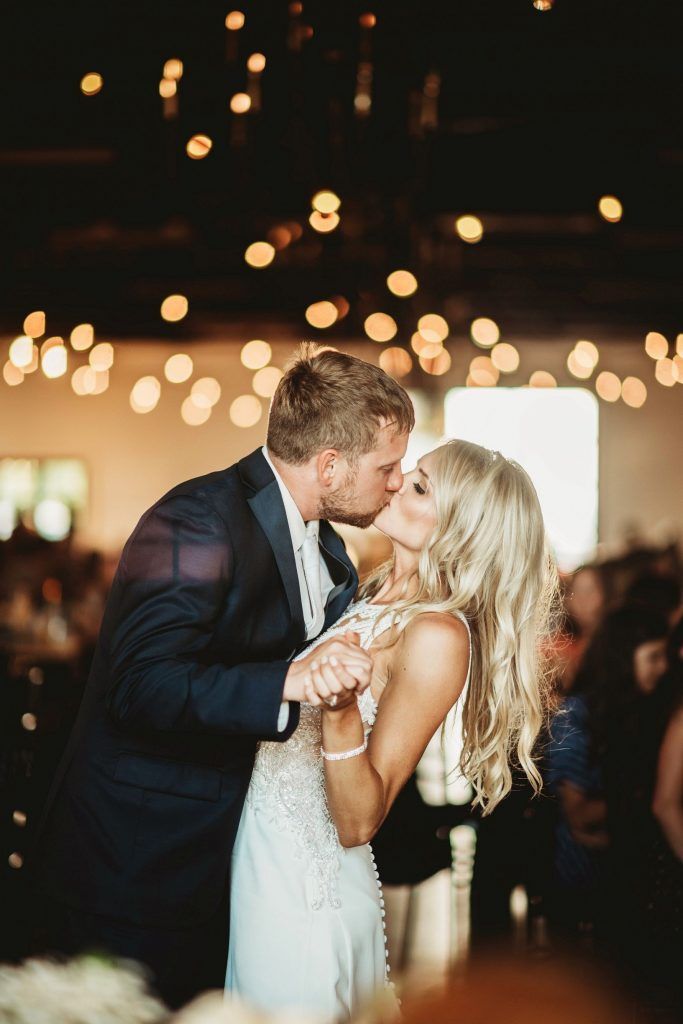 Couple kissing while dancing at wedding reception. Soft lighting and blurred background.