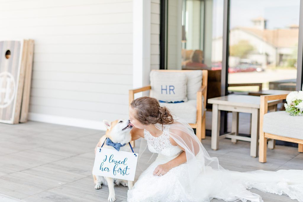 Bride kissing a dog wearing a bow tie and a sign that says,