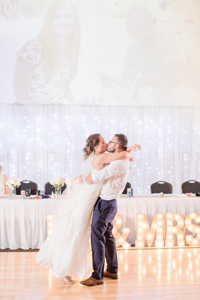 Couple embraces during first dance, venue lit with string lights and