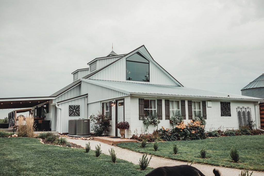 White barn with large window, porch, and landscaping under overcast sky.