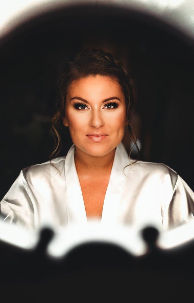 Woman in white robe with makeup, looking forward, framed by a lit circle.