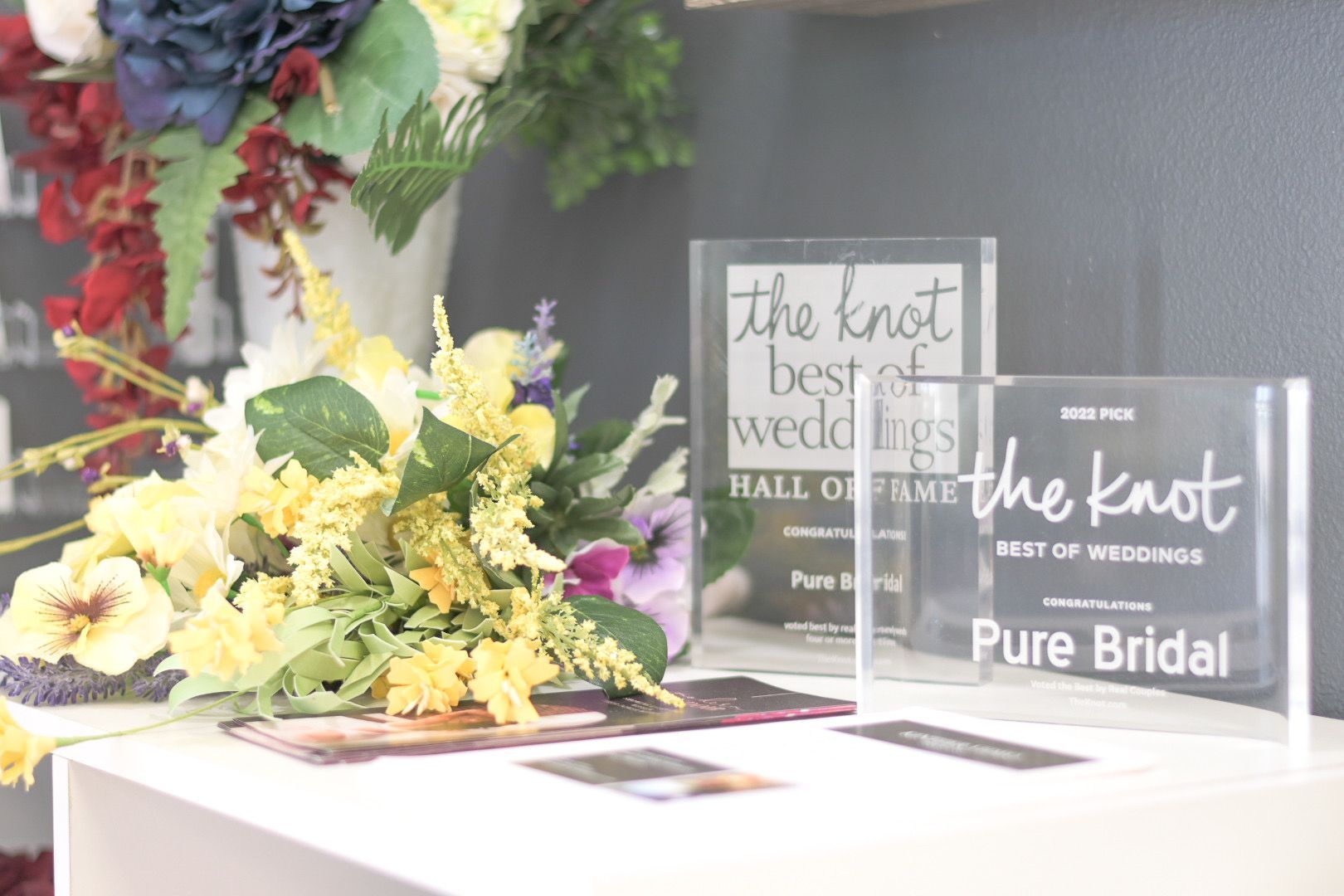 Woman in a white off-the-shoulder dress with a high slit, standing near a window.