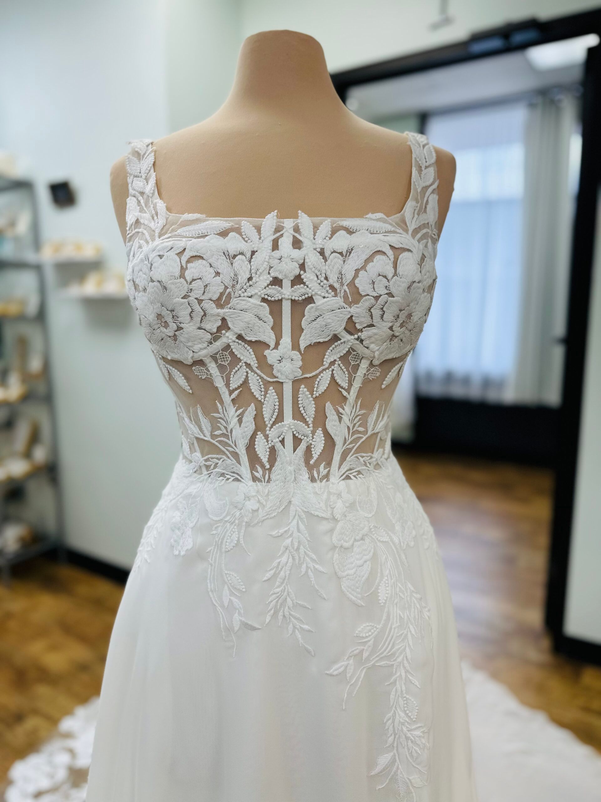 Wedding dress with square neckline and floral lace bodice displayed on a mannequin.