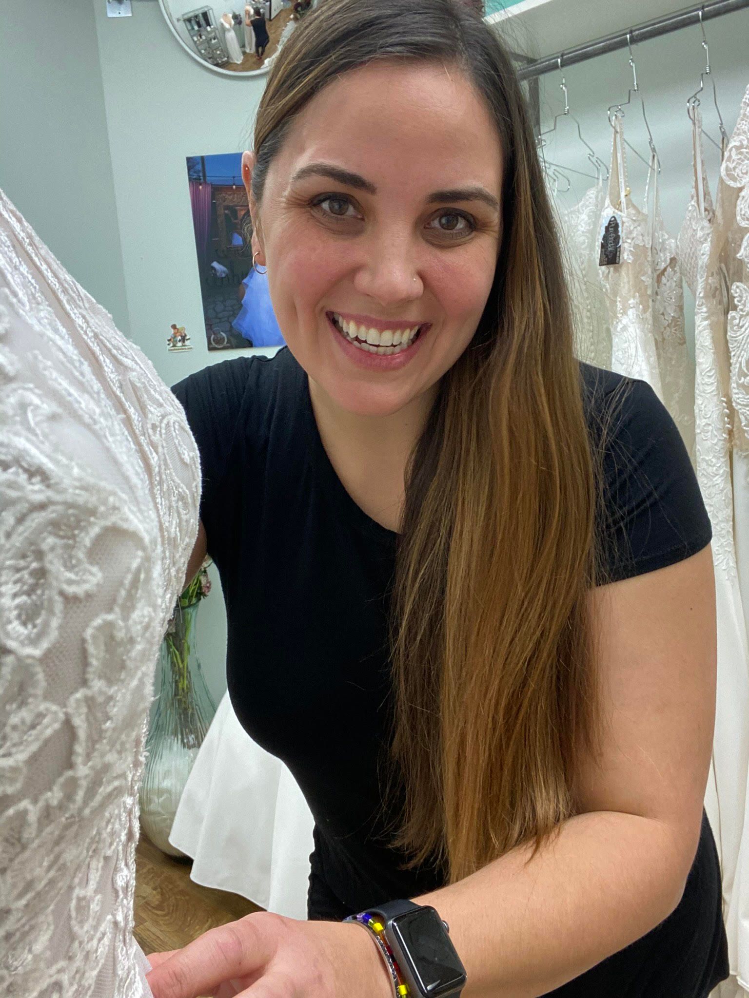 Woman smiles while adjusting a white wedding dress. Interior shop, dresses on display.