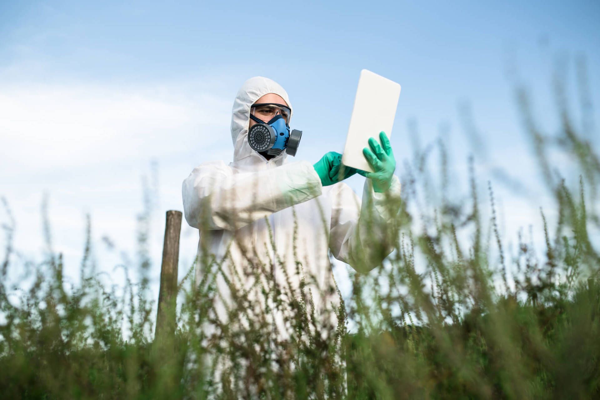 Person in hazmat suit examines a clipboard in a grassy outdoor setting.