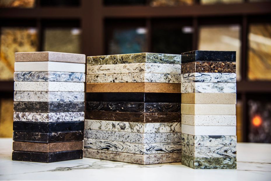 Tre blocchi campione di pietra impilati, nei colori grigio, nero e beige, su una superficie bianca.