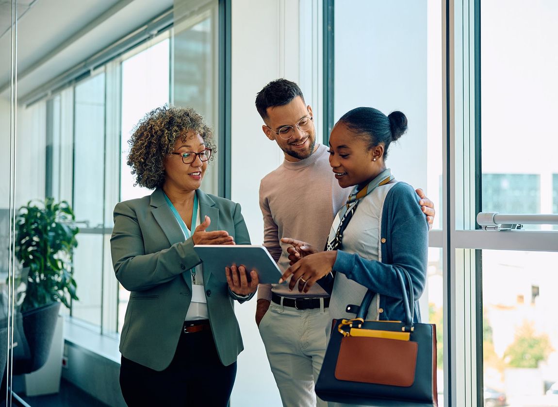 A group of people are standing next to each other in an office looking at a tablet.