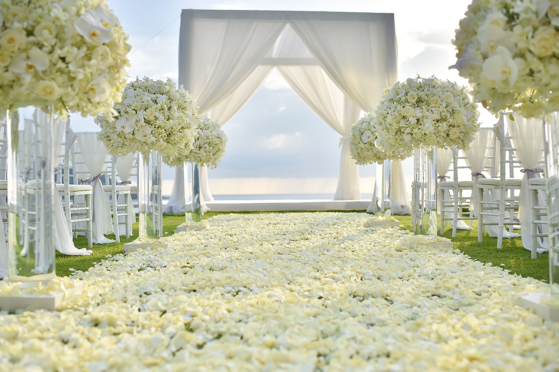 A wedding aisle decorated with white flowers and white chairs.