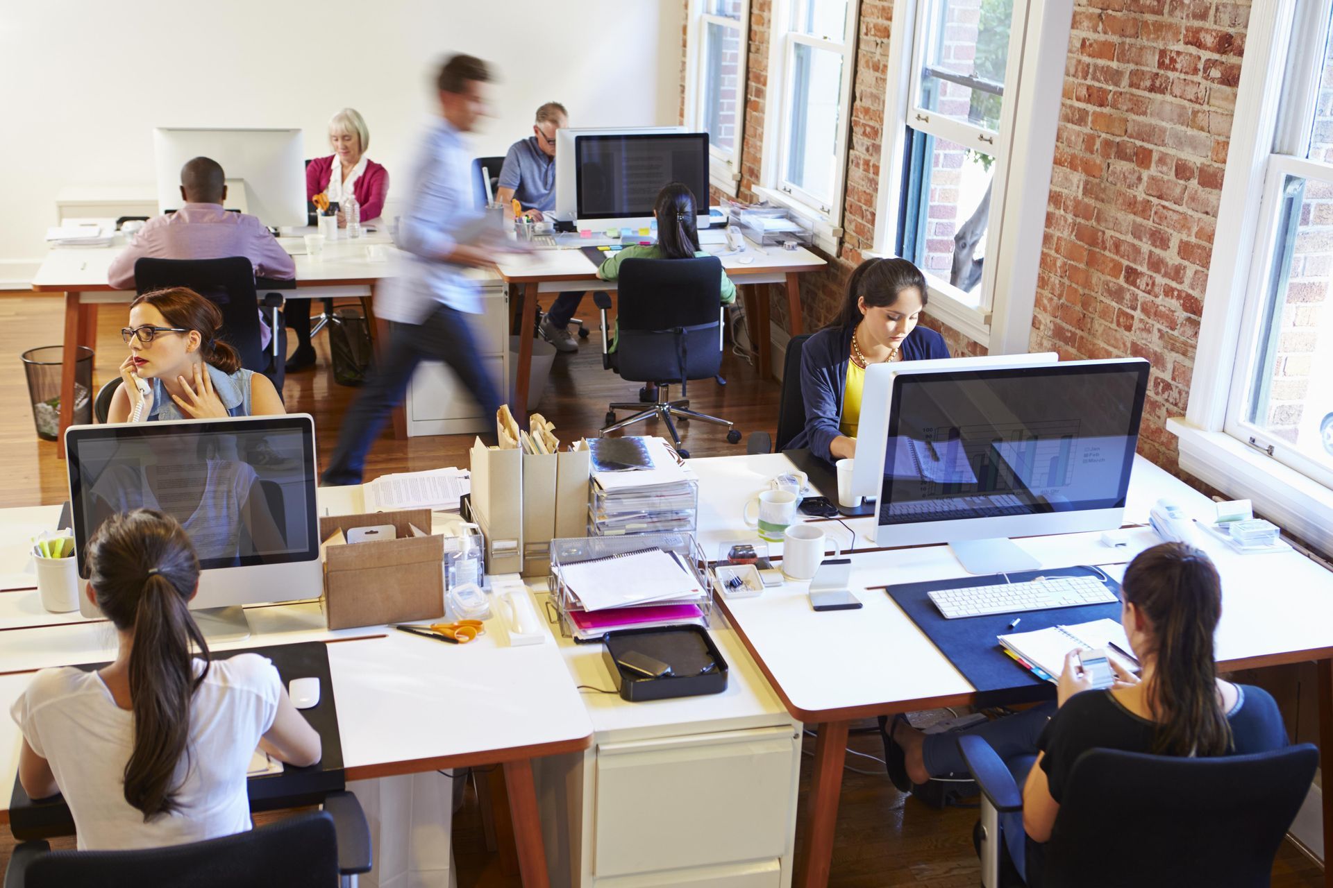 A group of people are sitting at desks in an office working on computers.