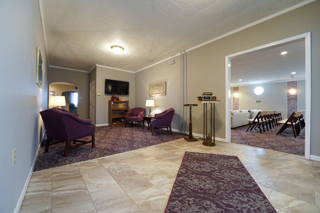 Lobby with purple chairs, rug, and a doorway leading to another room. Beige and gray walls.