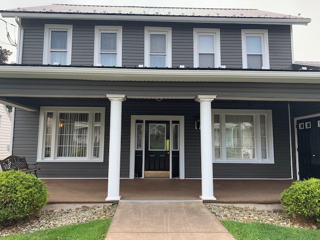 Gray two-story house with white columns, windows, and front door.  Green bushes and grass.