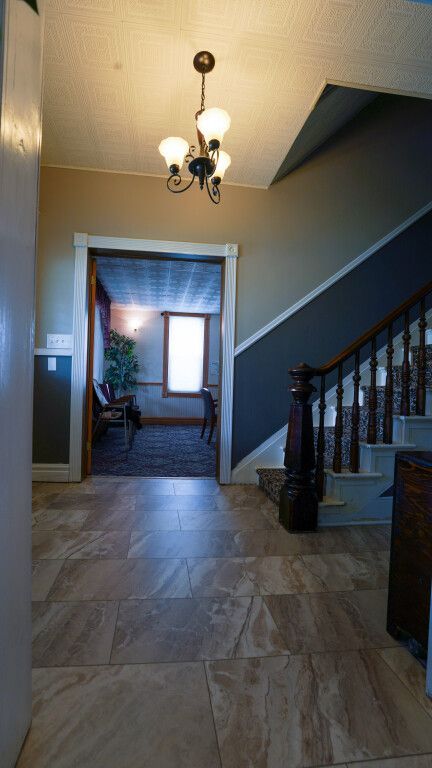 Hallway with stairs, tiled floor, and doorway to a room with a window, antique light fixture.
