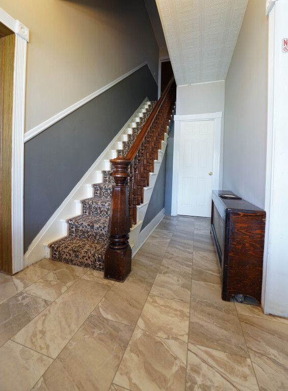 Staircase with dark wood banister and gray wall, leading upstairs from a tiled hallway.