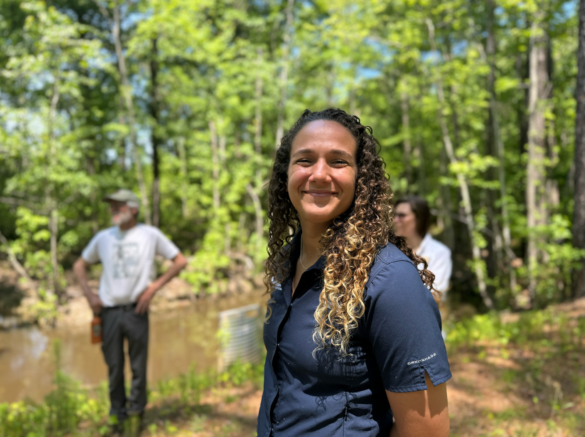 A land trust professional is standing in the woods next to a river.