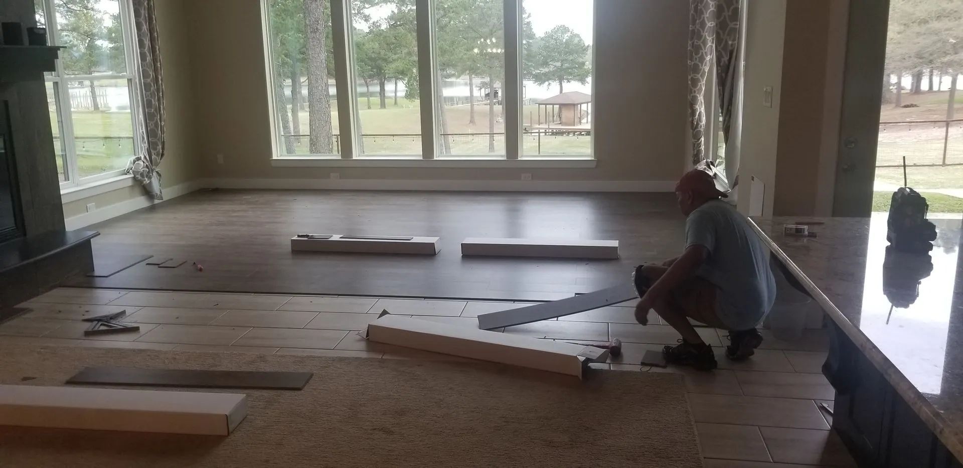 A man is installing hardwood flooring in a living room.