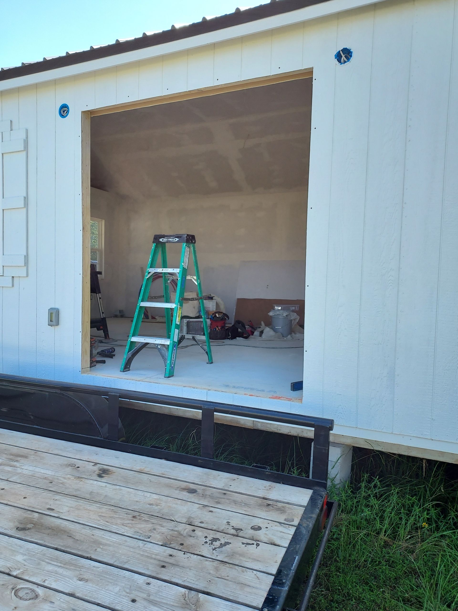 A ladder is sitting on the side of a building next to a trailer.