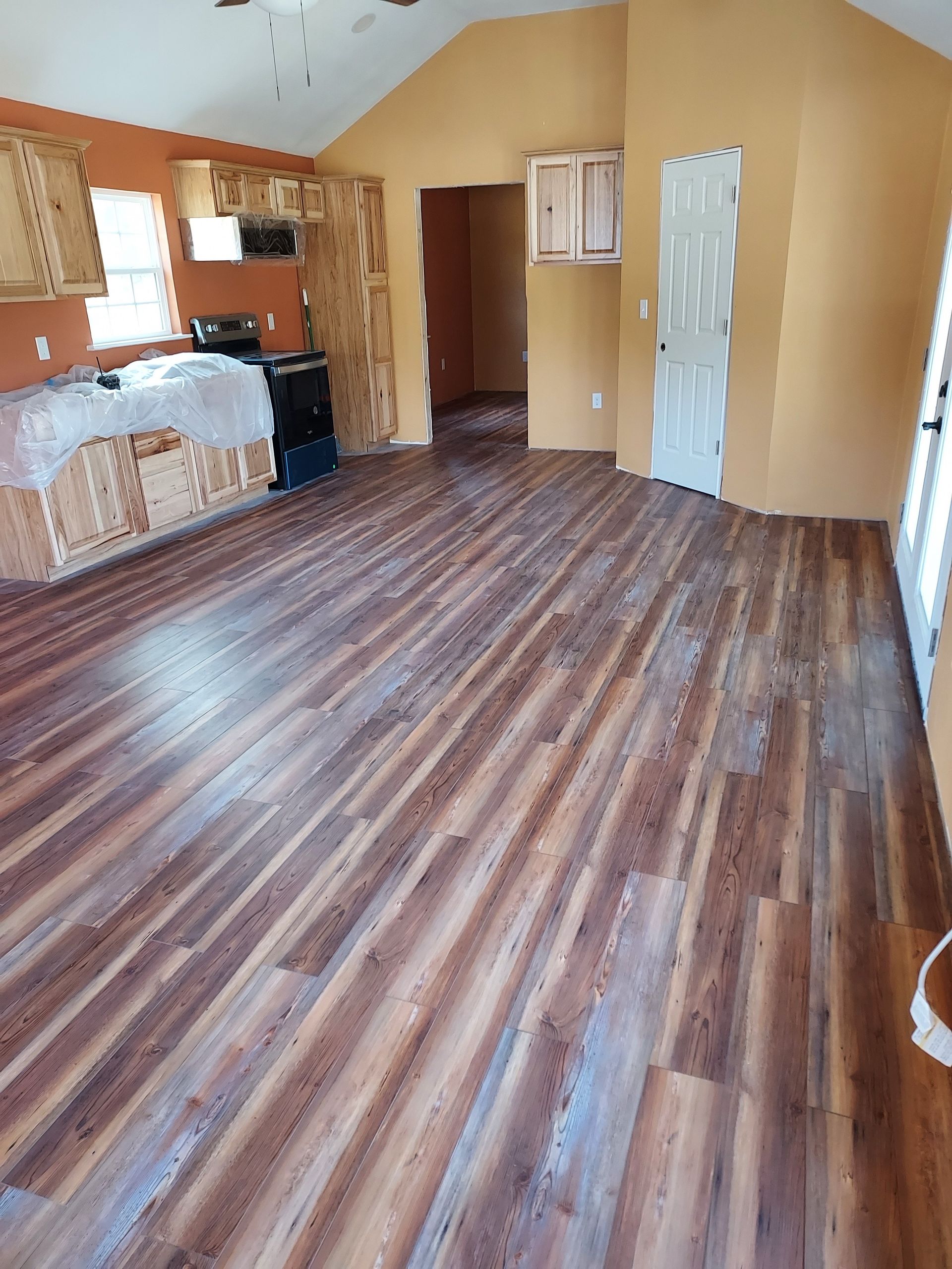 A living room with hardwood floors and a kitchen in the background.
