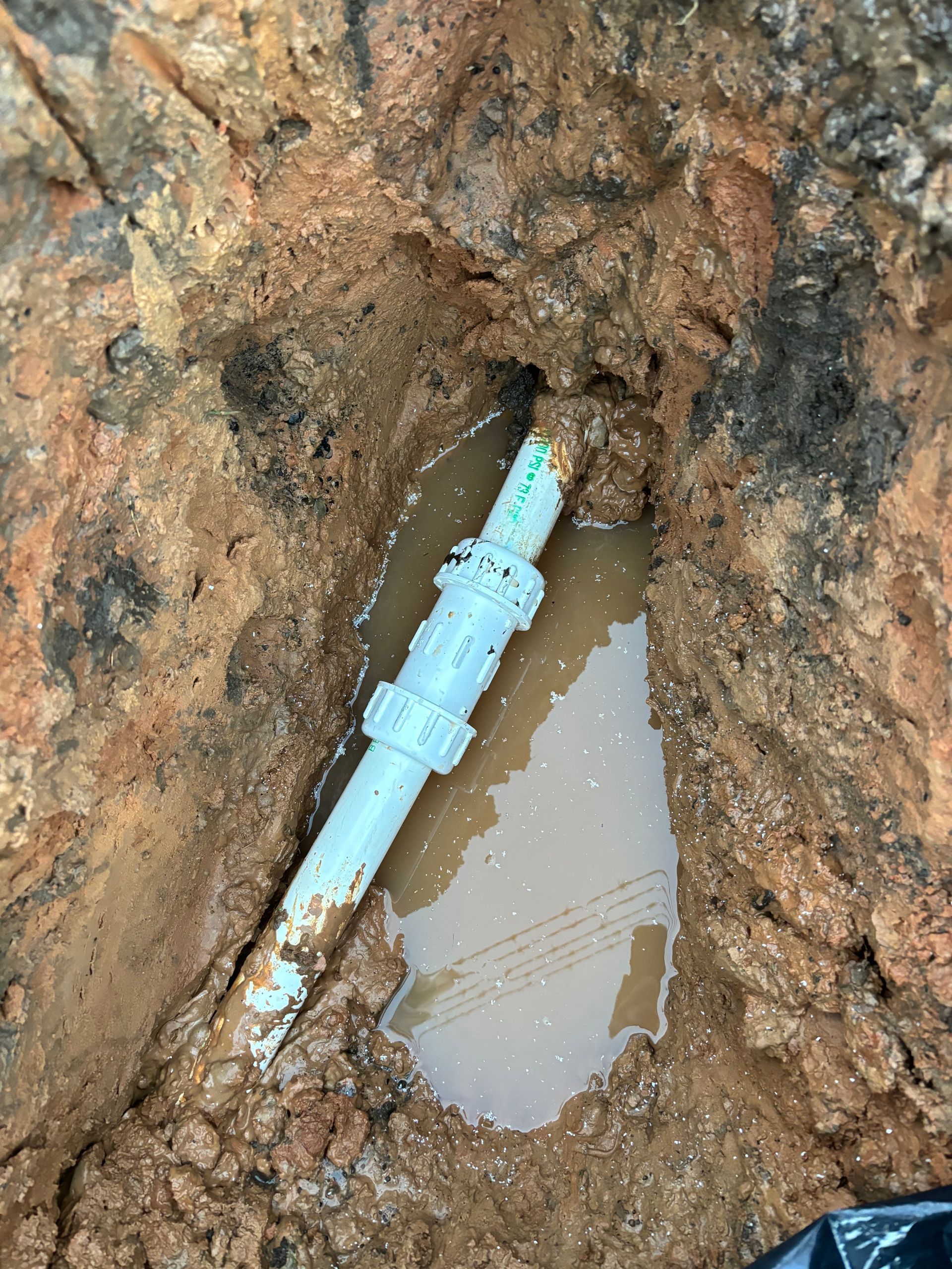A white pipe is laying in the dirt next to a puddle of water.