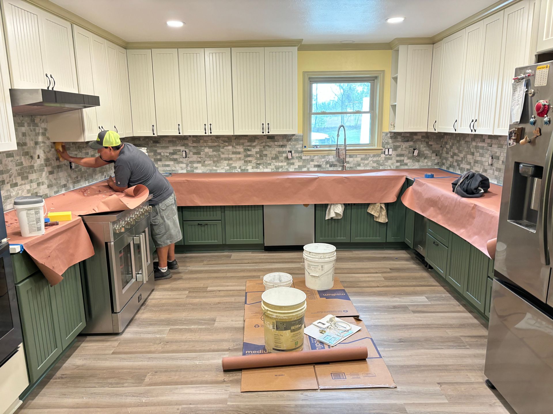 A man is laying tile in a kitchen.
