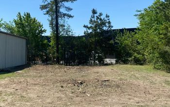 A large dirt field with trees and a building in the background.