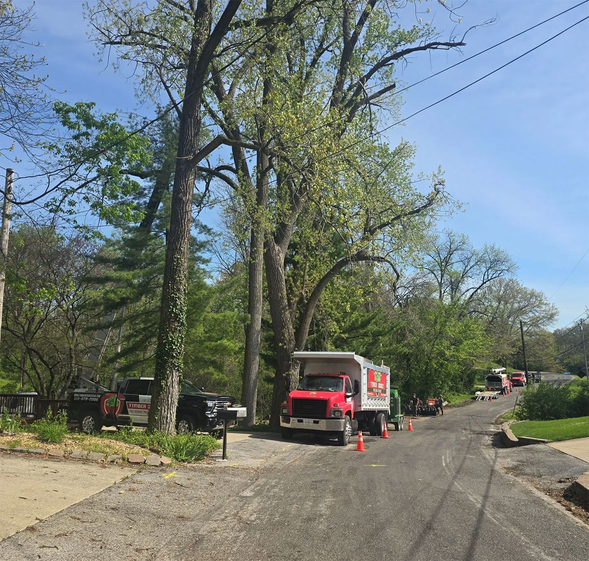 Red truck parked on a narrow road with other vehicles and trees; cones set up to block the road.