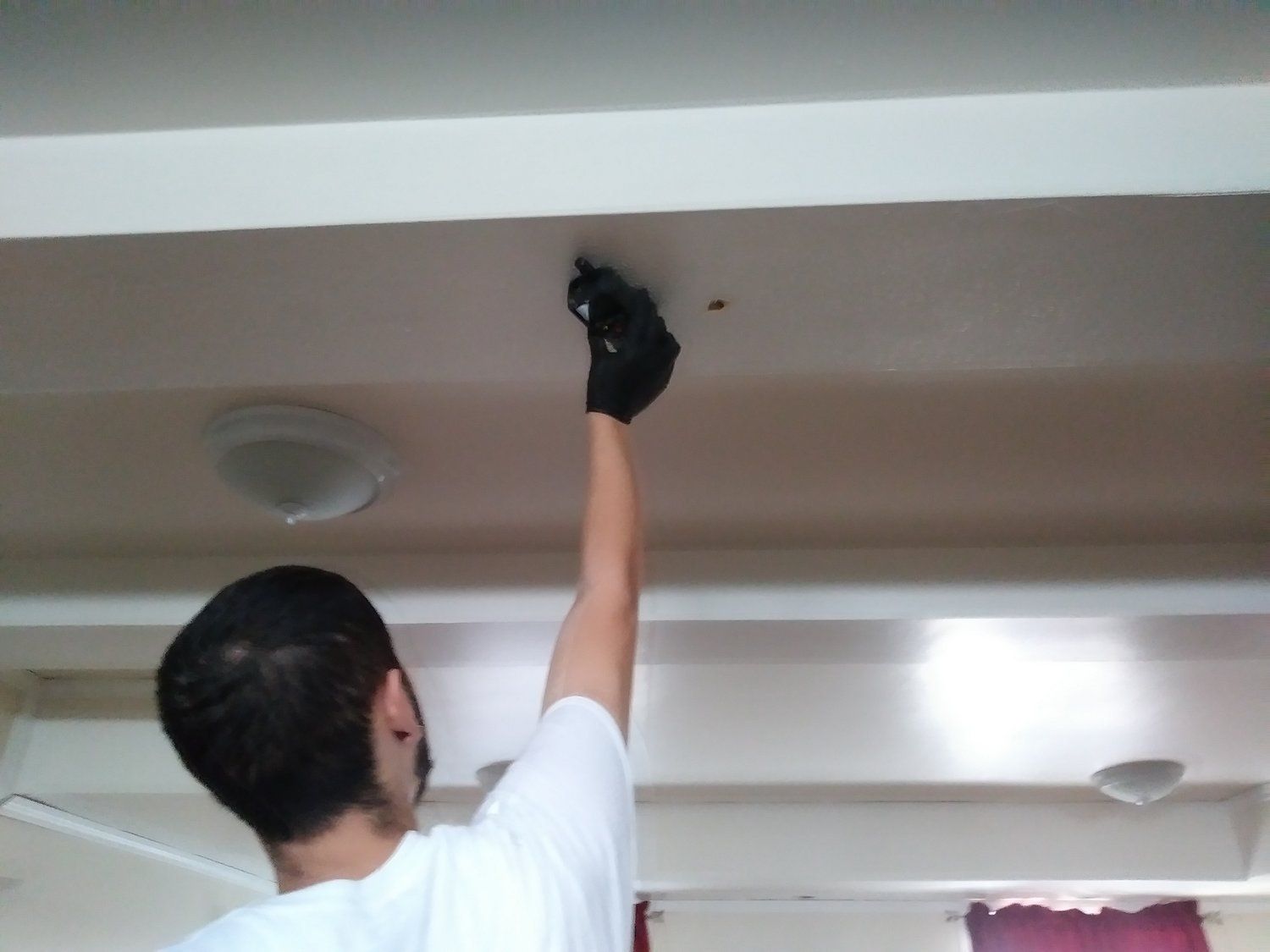 A man in a white shirt is reaching for something on the ceiling