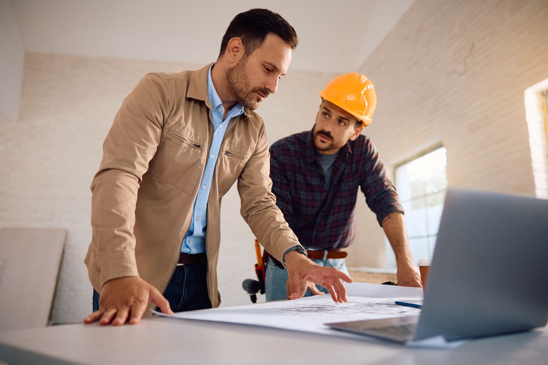 Two men in hard hats are looking at a laptop computer.