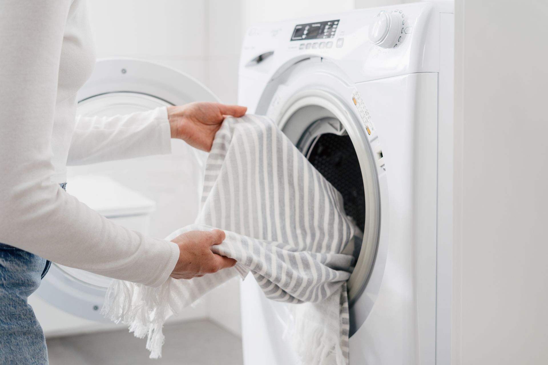 A woman is putting clothes in a washing machine.