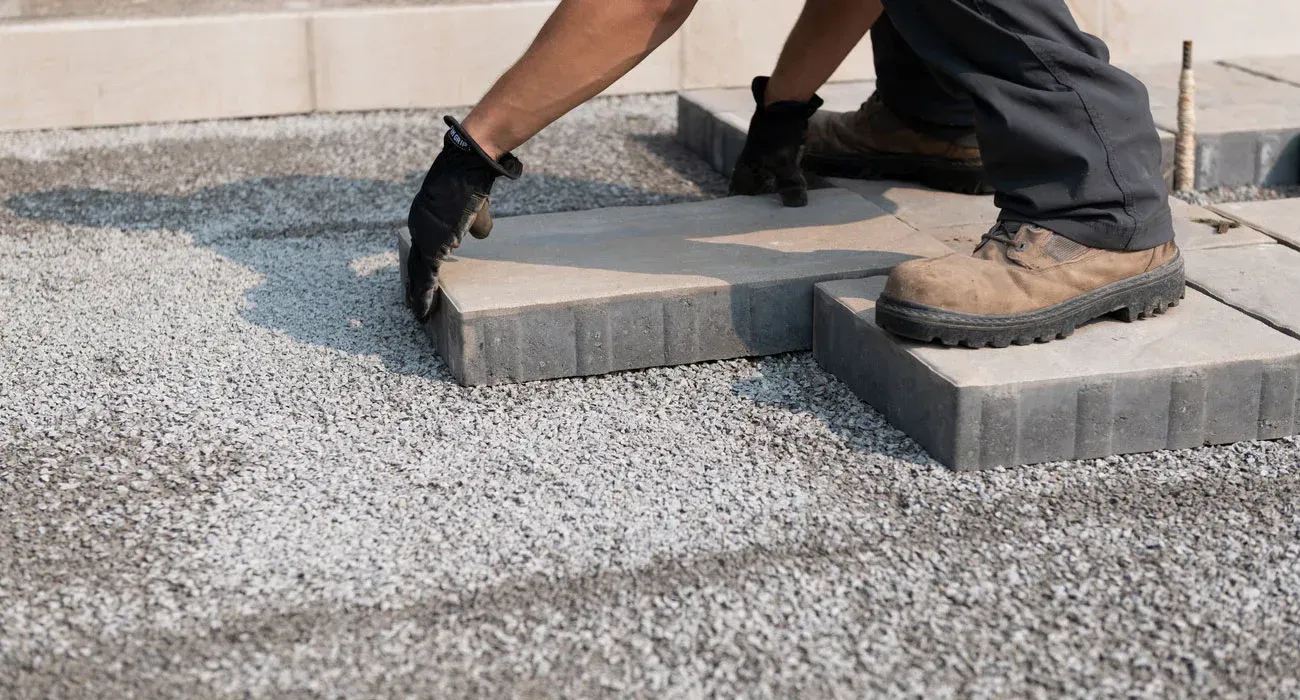 Person wearing gloves placing a paving stone on gravel base in Wilmington North Carolina.