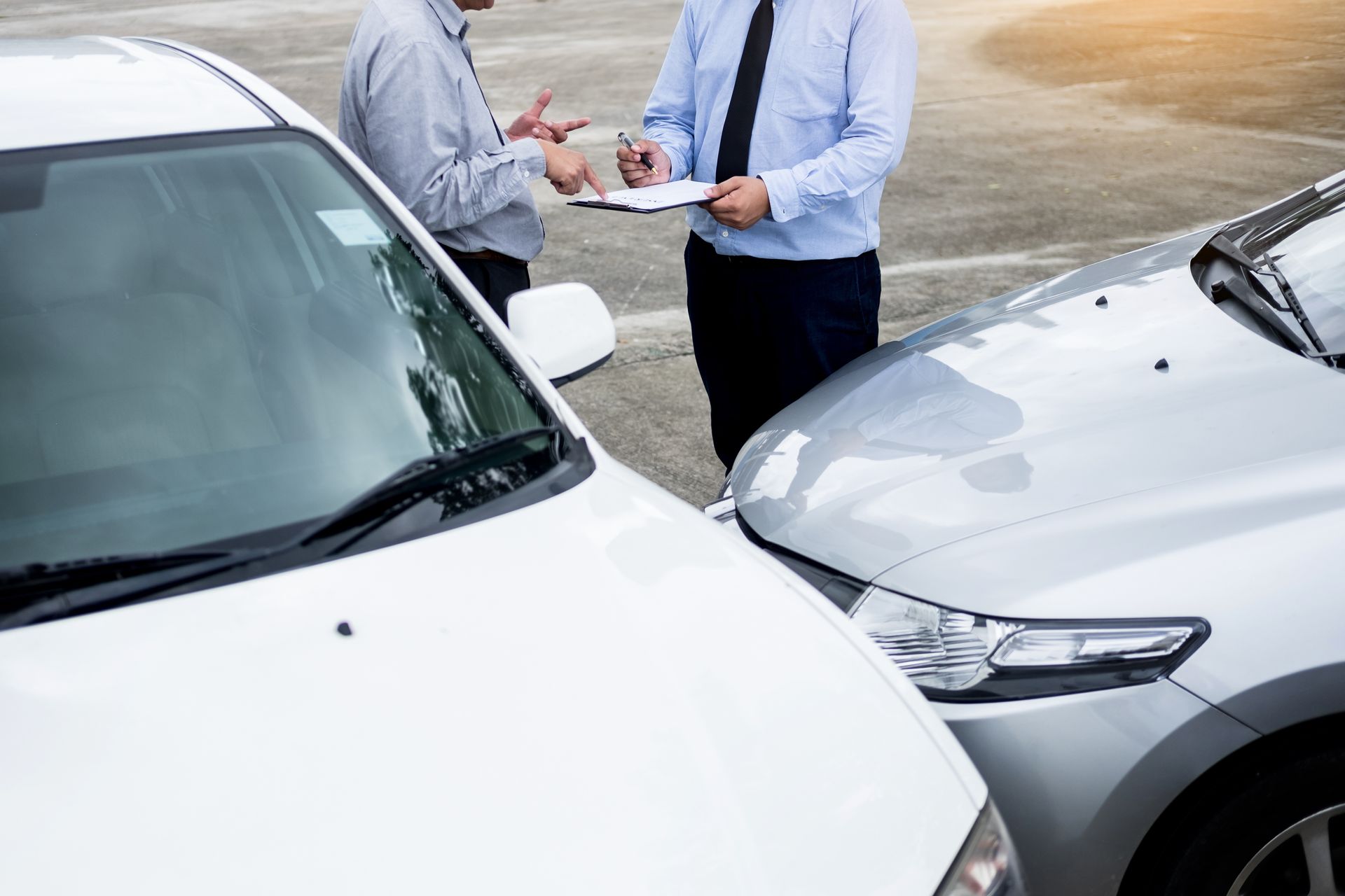 Two people discussing paperwork between two parked cars after a minor collision