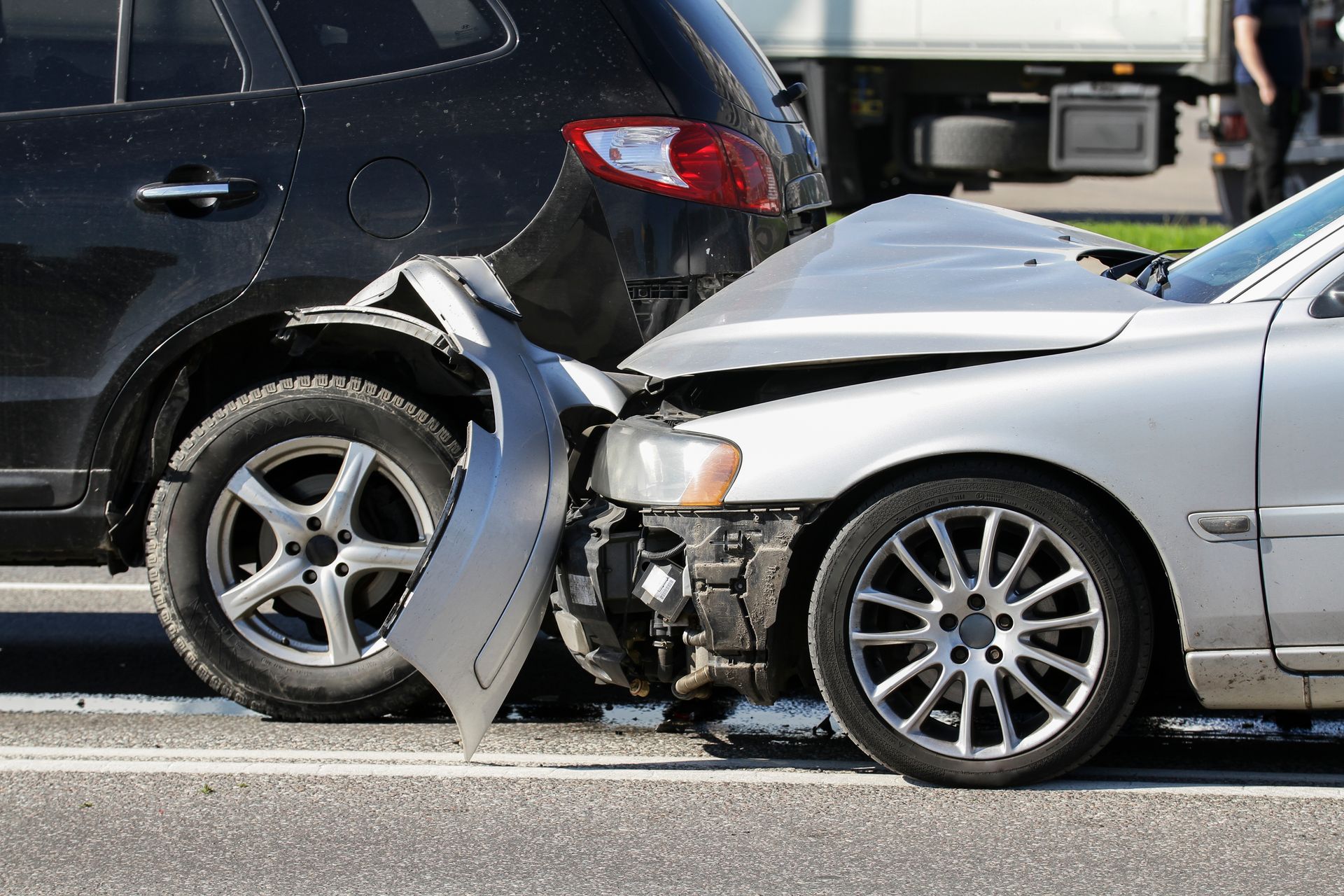Two cars involved in a front-end collision, with a silver car’s hood crumpled and bumper detached.