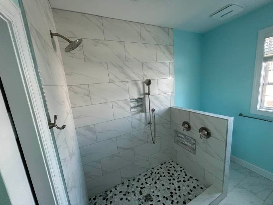 A walk-in shower with marble-look wall tiles, a pebble floor, a rain showerhead, a handheld sprayer, and blue walls.