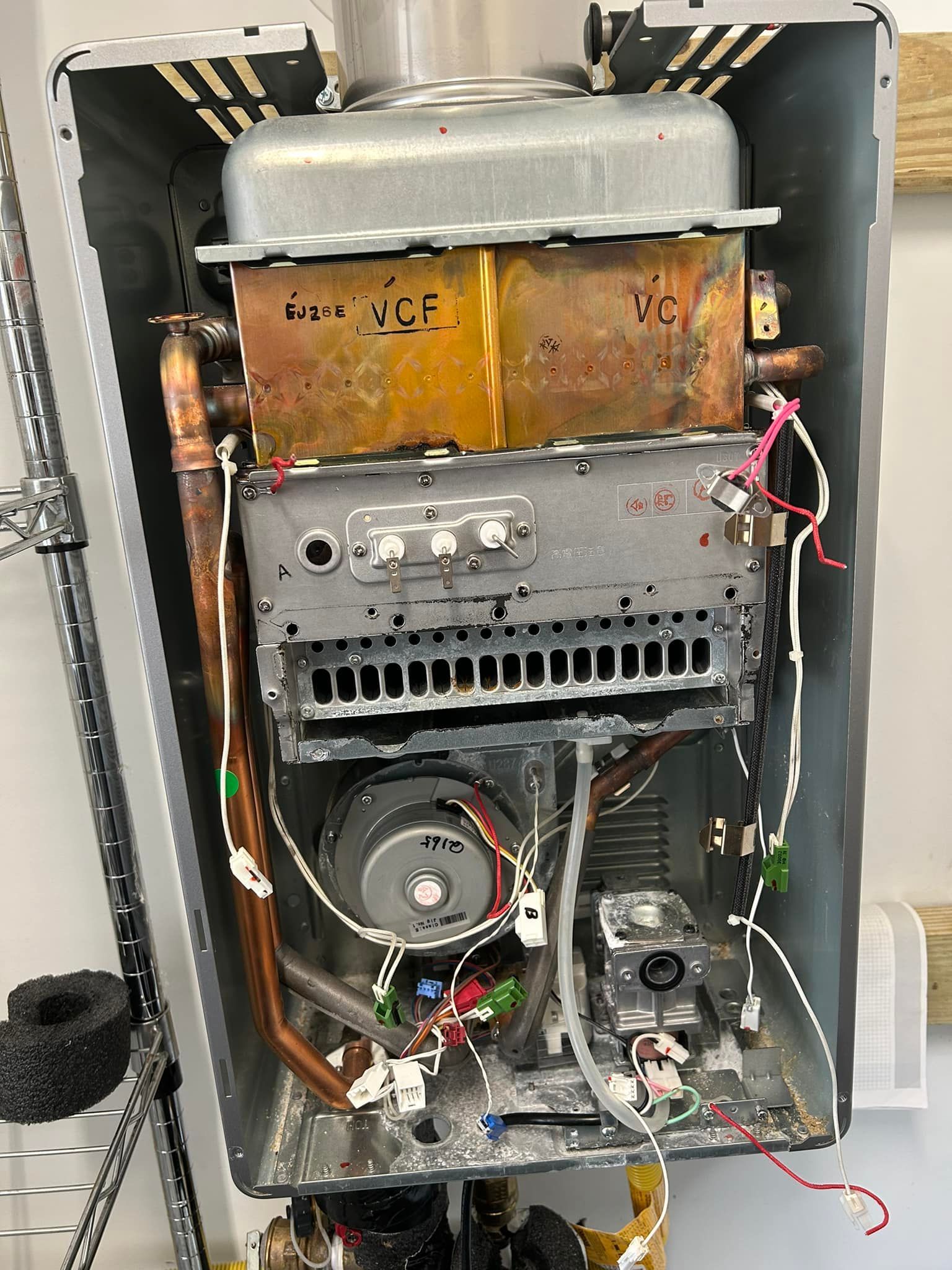 Internal view of a tankless water heater with visible copper heat exchanger, gas burner assembly, and internal wiring.