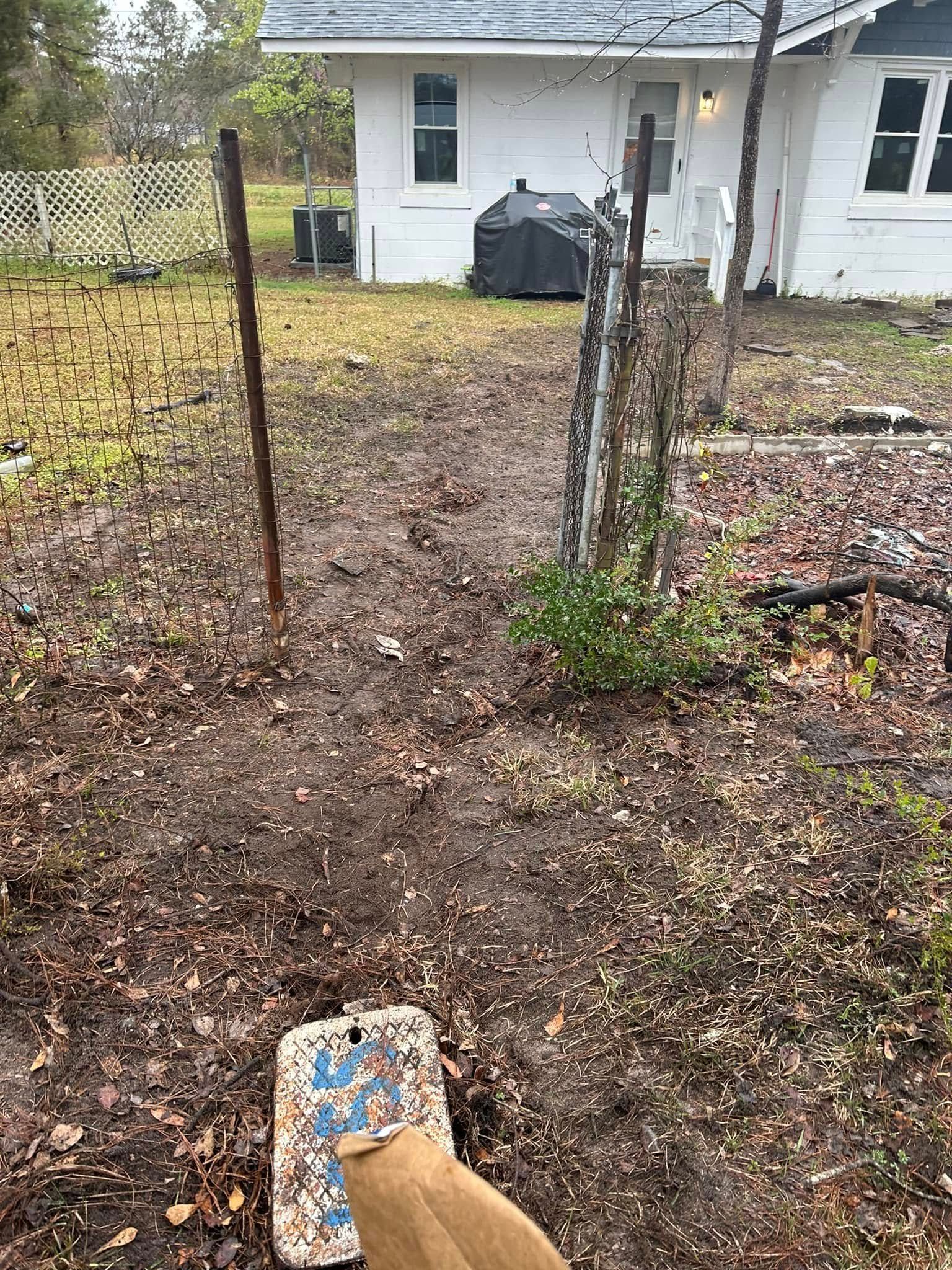 A muddy backyard leads toward a white house with a covered grill on the lawn and a blue marker in the foreground.