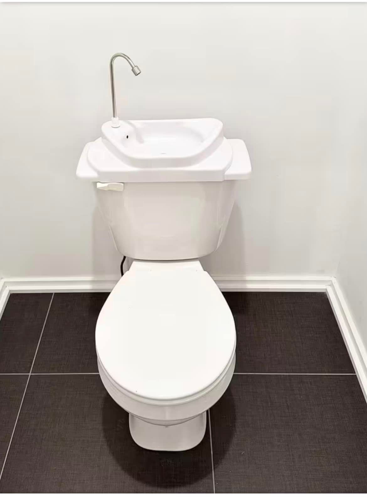 A white toilet with a sink basin integrated into its tank lid, featuring a small faucet, set against a tiled floor.