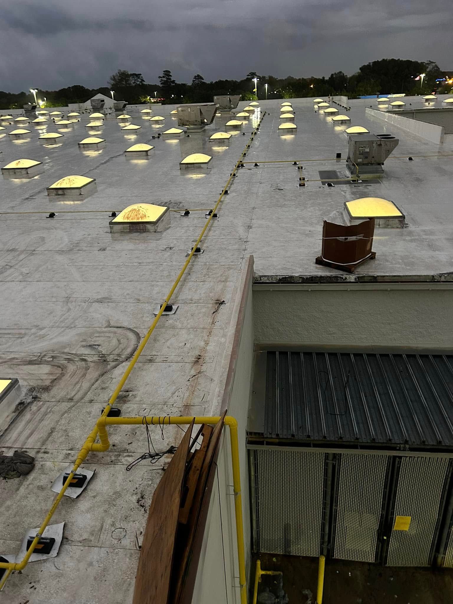 A yellow gas pipe runs across a commercial rooftop with numerous skylights and a large HVAC unit at dusk.