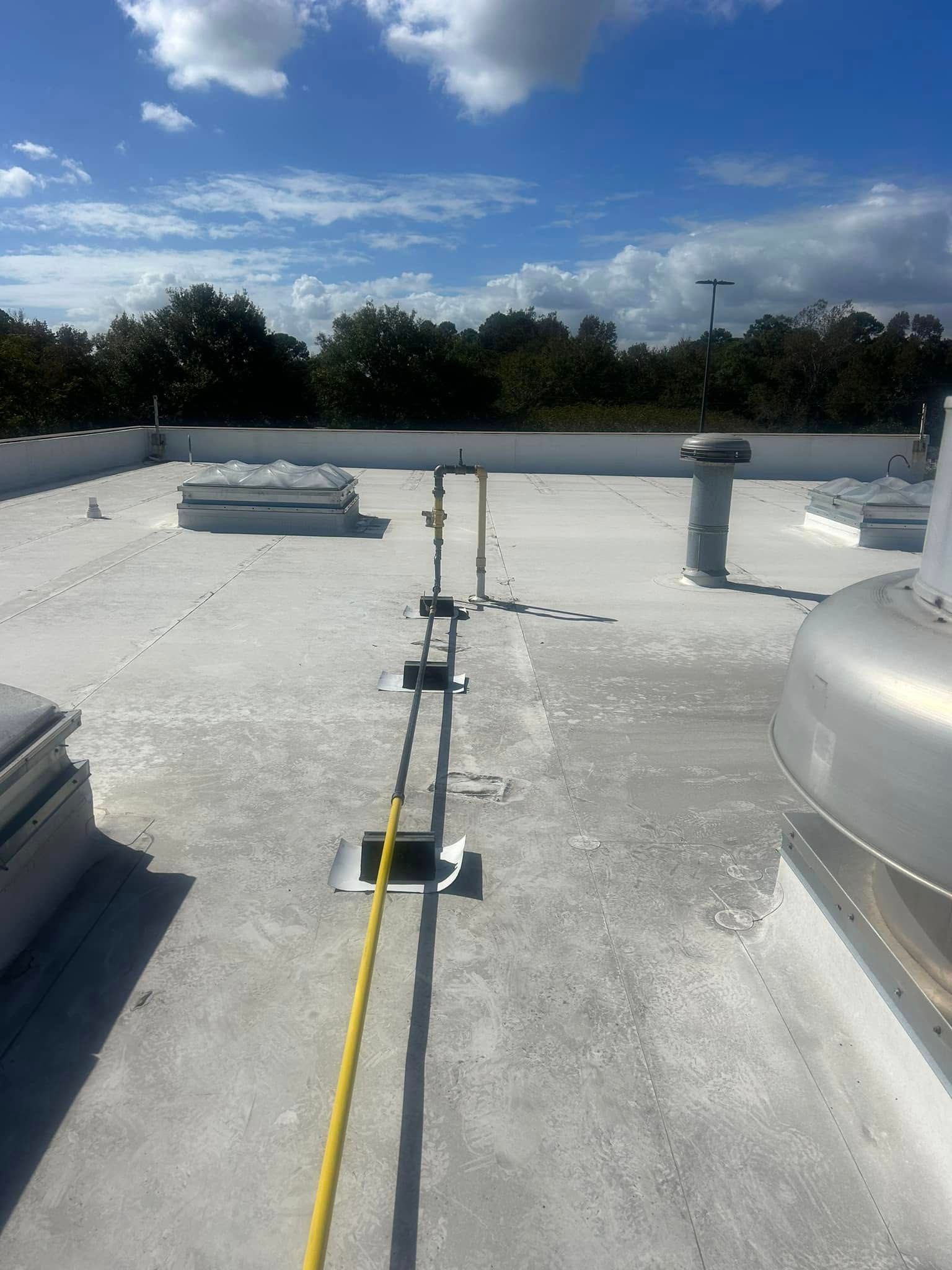 A flat, white roof featuring a yellow utility pipe running along the center, supported by blocks against a blue sky.