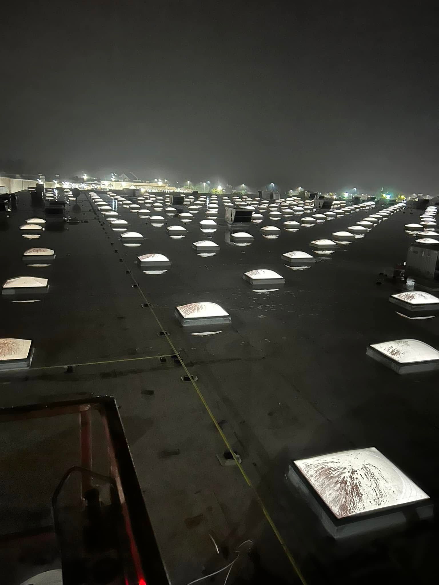 A high-angle night view of a flat, dark roof featuring numerous square skylights arranged in a grid pattern.
