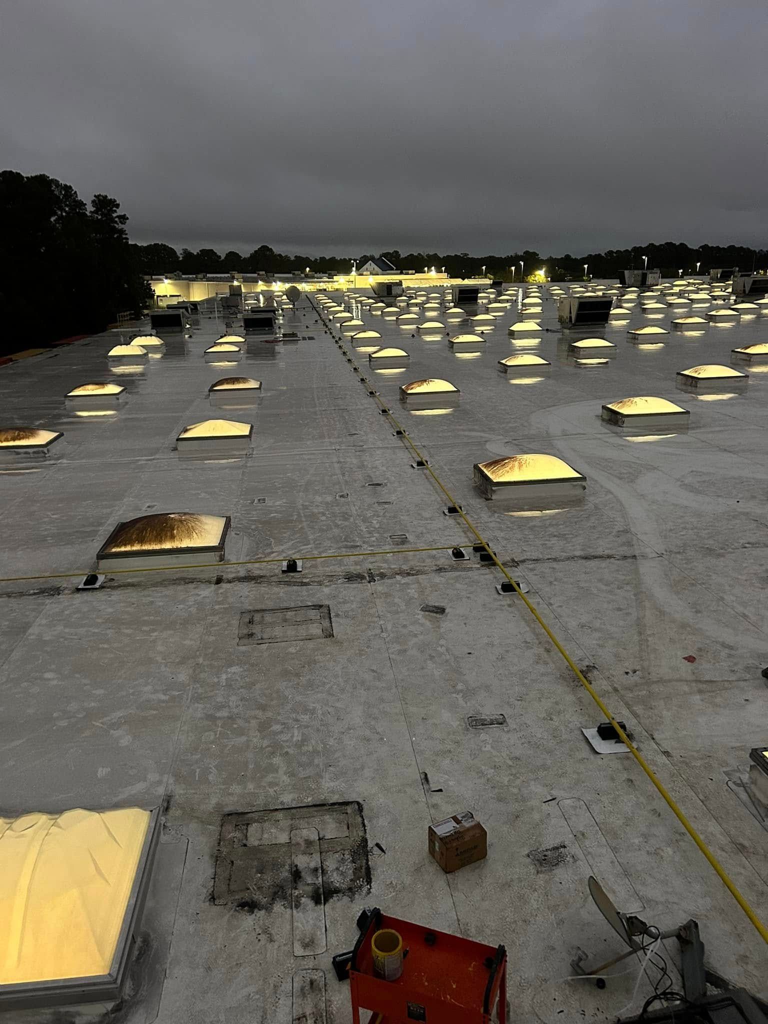 A flat commercial roof at dusk, featuring numerous skylights, a red cart, and a yellow measuring tape.