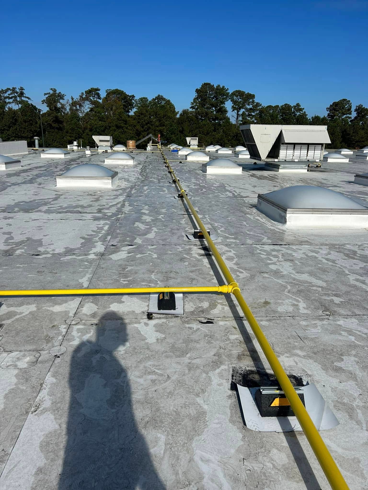 A yellow pipe runs across a flat roof filled with dome skylights under a clear blue sky.