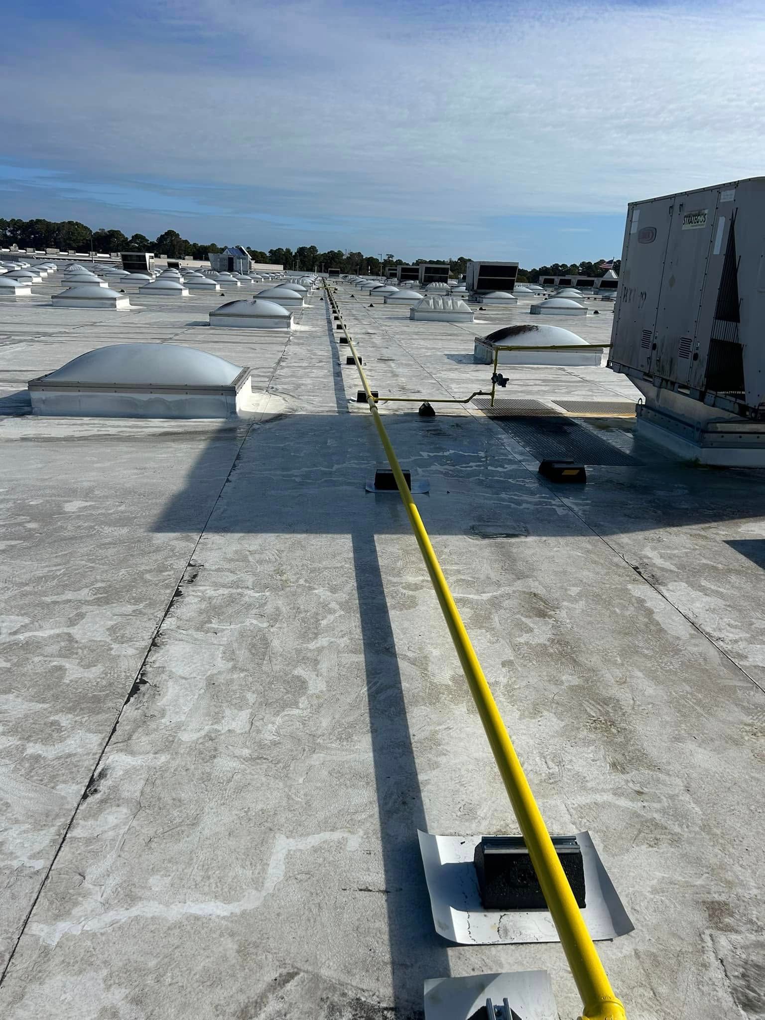 A yellow gas line runs across a flat industrial roof with numerous skylights and mechanical equipment under a blue sky.