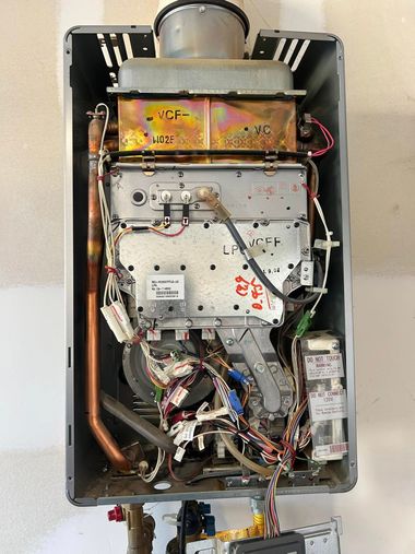 The interior components of a wall-mounted gas tankless water heater, showing copper pipes, wiring, and metal housing.