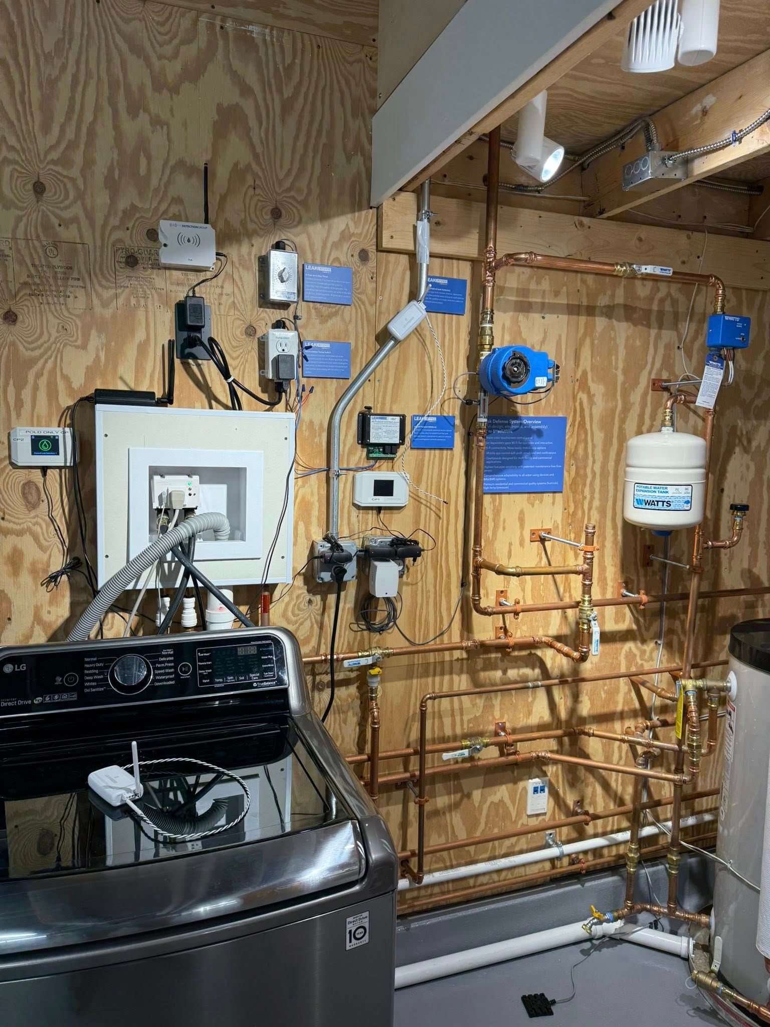 Utility room with a washing machine next to a wall featuring exposed copper plumbing, electrical panels, and sensors.