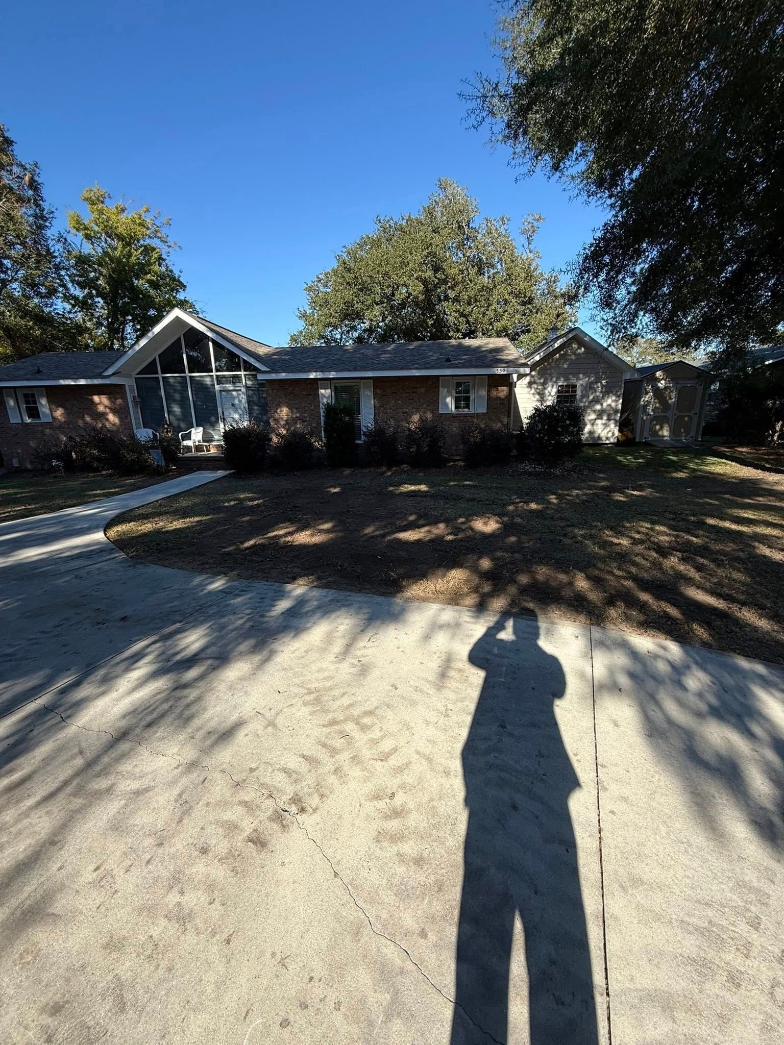 A single-story brick house with a concrete driveway in the foreground, under a clear blue sky on a sunny day.