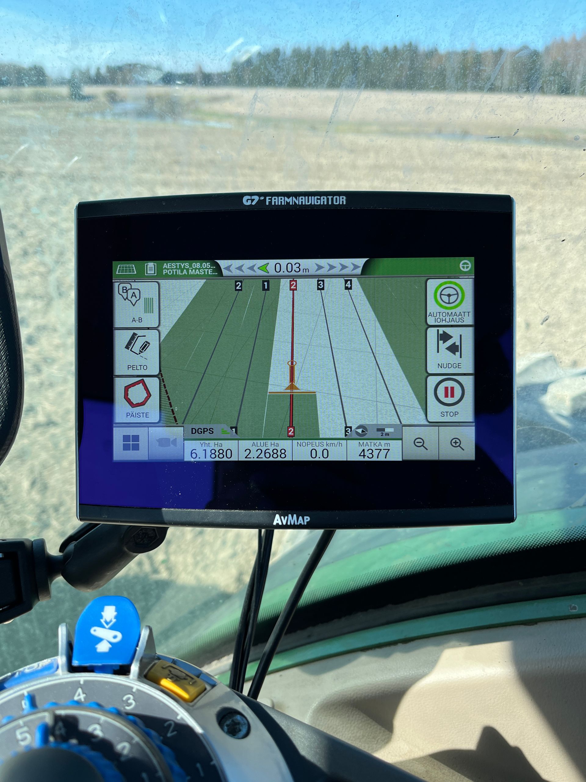 Traktorin ohjaamon GPS-näytössä näkyy vihreä kenttä, jossa on valkoisia viivoja, ja toiminnanohjauskuvakkeet.