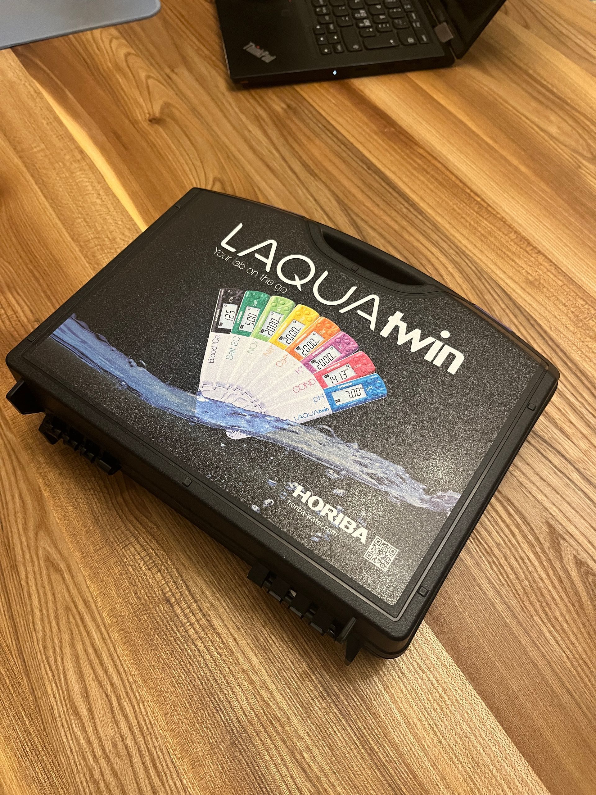 A black case is sitting on a wooden table next to a laptop.