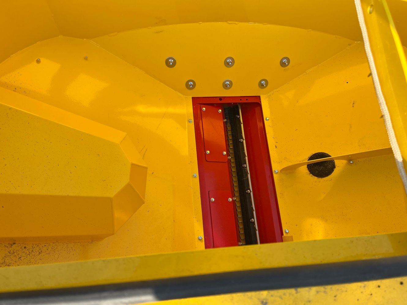 Teollisuuskoneen keltainen sisäosa, punainen keskiosa, pultit ja tumma reikä.