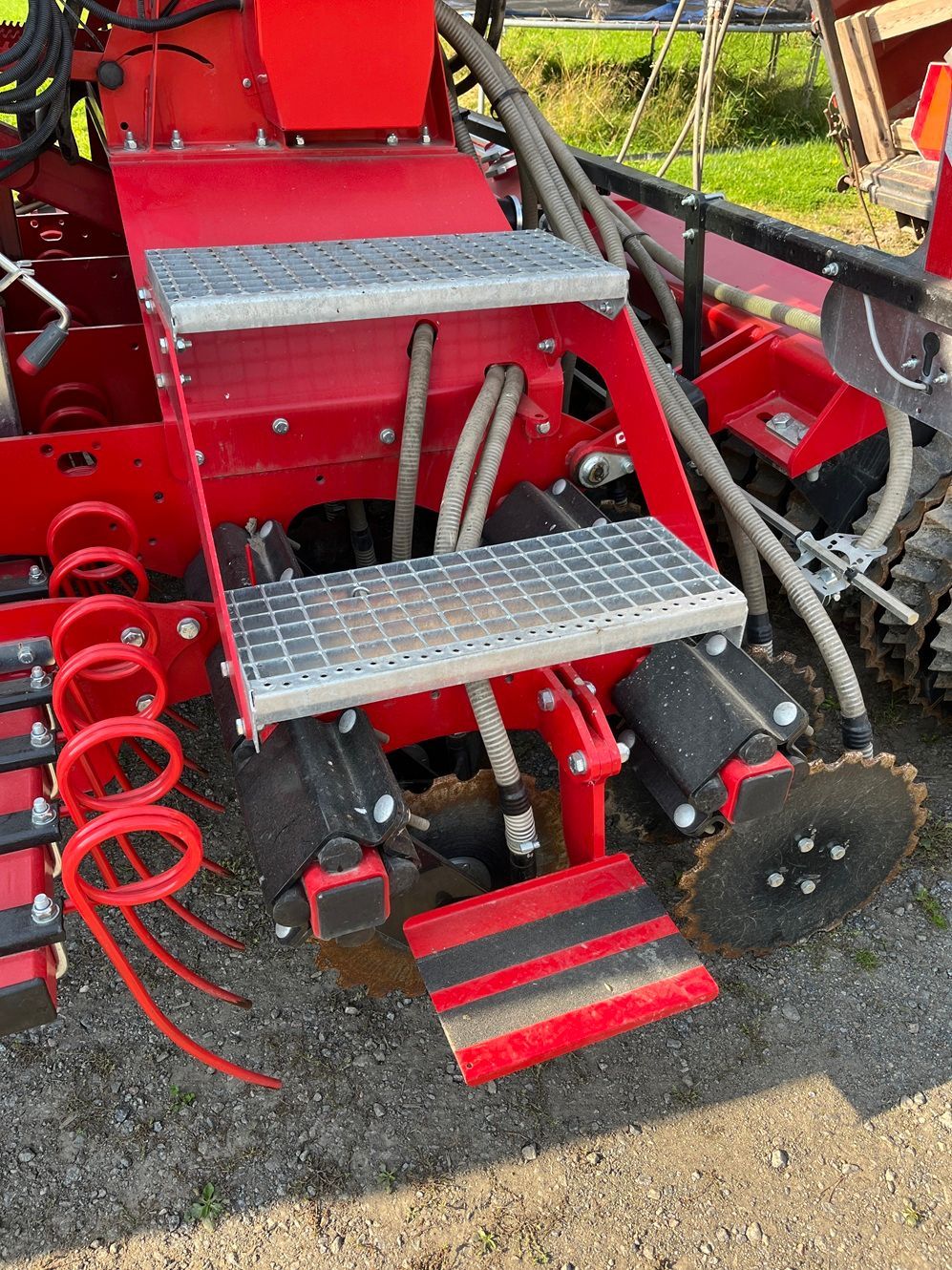 Punainen maatalouskone, jossa on metalliset askelmat ja letkut.