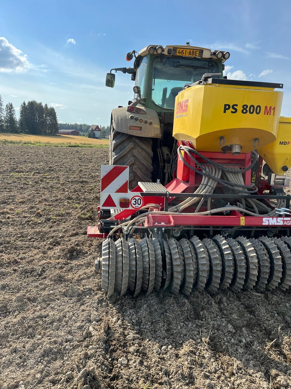 Traktori ja kylvökone pellolla; kone kylvää siemeniä ulkona.